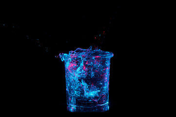 Rocks glass overflowing with water under bright blue lights with red on a black background