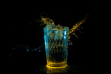 Artistic splash of water from a vintage glass under blue and yellow lights isolated on a black background