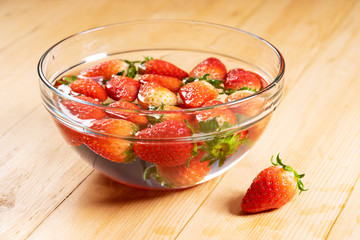 Fresh strawberries in water bowl on wooden table