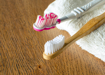 Bamboo toothbrush vs plastic toothbrush with towel on the wooden background