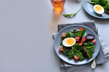 Salad mix with spinach, arugula,beet leaves, tomatoes and eggs on gray wooden background. Vegetarian food concept. Selective focus.