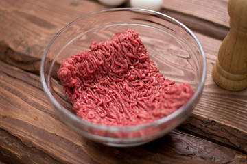 Fresh minced meat on a plate on a wooden background for cooking.