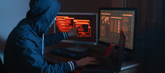 Hacker in the hood is pointing his finger at the display indicating the location of the cyberattack