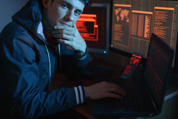 Man in the hood looking in the camera. Hacker attacks and online fraud in the dark on the screen...