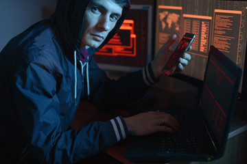 Man in the hood looking in the camera. Hacker attacks and online fraud in the dark on the screen...