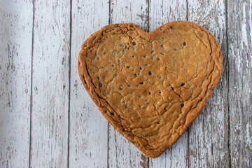 Huge Heart-shaped chocolate chip cookie on rustic wood table with copy space