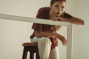 attractive woman in retro outfit posing on stool with big white frame isolated on beige