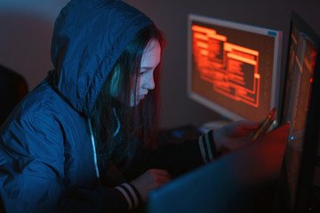 Girl hacker in the hood holding the phone in hands trying to hack the mobile device cloud in the...