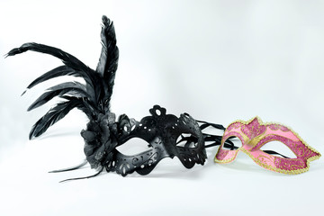 Two Venetian masks, one pink and one black on a white background