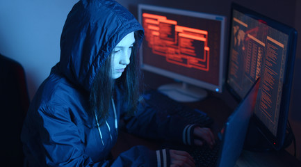 Girl hacker in a hood typing program code while committing a cybercrime hacking a firewall on the...