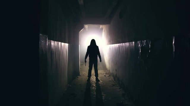 Silhouette of man maniac or killer or horror murderer with knife in hand in dark creepy and spooky corridor. Criminal robber or rapist concept in thriller atmosphere