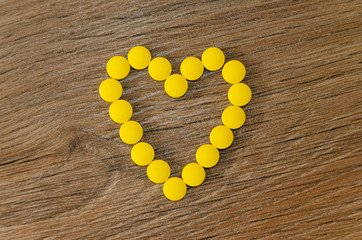 Heart shaped of yellow pills on wood background