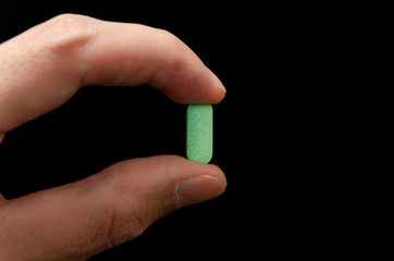 A man's hand holding a e pill between thumb and forefinger on a black background. Prescripted medication: painkillers, light narcotics, antibiotics.