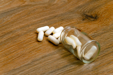 Composition of white capsule and a jar on the wood background