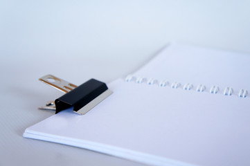 Black color bulldog clip clipping small white notebook and isolated on white background. 
