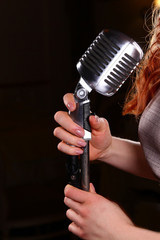 Hands of the singer holding a large shiny metal microphone on a black background. A place for a label, copy space for text