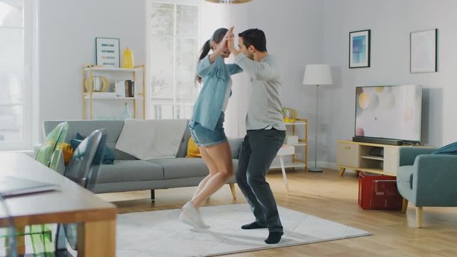 Happy Beautiful Couple is Having Fun and Actively Dancing in their Cozy Living Room at Home