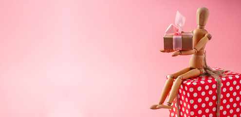 Wooden toy model holding gifts on pink background. Holiday card for Valentine's day and women's day. Place for text