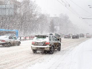 cars drive at snow-covered road in snow blizzard