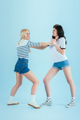 Aggressive girls in denim shorts fighting on blue background