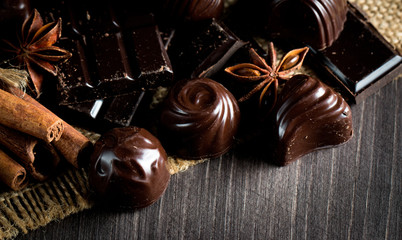 Assortment of dark, white and milk chocolate stack, chips. Chocolate and coffee beans on rustic wooden sacking background. Spices, cinnamon. Selective macro focus. Chocolates background. Sweets
