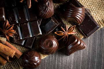 Assortment of dark, white and milk chocolate stack, chips. Chocolate and coffee beans on rustic wooden sacking background. Spices, cinnamon. Selective macro focus. Chocolates background. Sweets