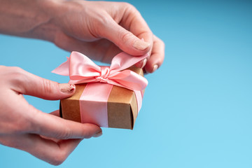 Hands holding gift box Packed in Kraft paper with pink ribbon on blue background. Card for Valentine's and women's day