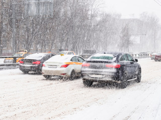 cars drive at snow-covered urban road in snowstorm