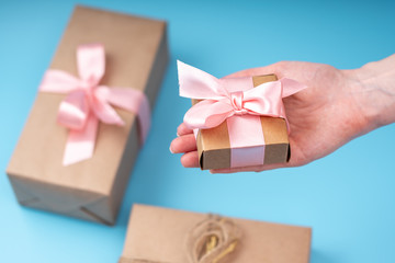 Women's hands holding gift box Packed in Kraft paper with pink ribbon on blue background. Card for Valentine's day