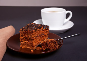 Delicious chocolate cake on the brown plate with cup of coffee on the black table
