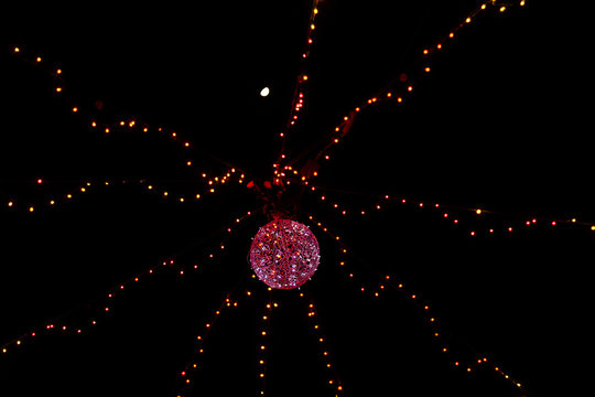 Iluminación navideña de noche con luces de colores, bola de luz en el centro y la luna en lo alto