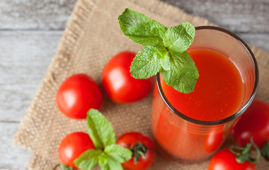 Close-up of a glass of tomato juice with vegetables on wooden sacking background. Vitamins and minerals. Healthy drink concept.