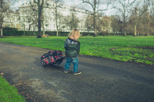Little toddler pulling suitcase in the park