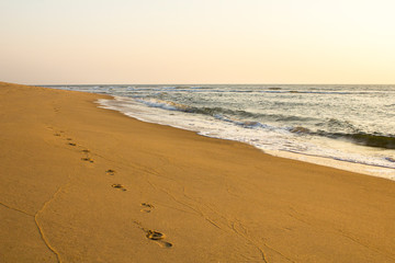 human footprints on the yellow sand against the background of the sea and gray sky in the evening