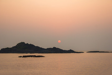 rocks in the sea against a purple pink sky of sunset and sun above the horizon