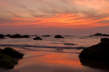 Fototapeta na wymiar sandy beach on the background of rocks in the sea and bright orange pink purple sunset sky