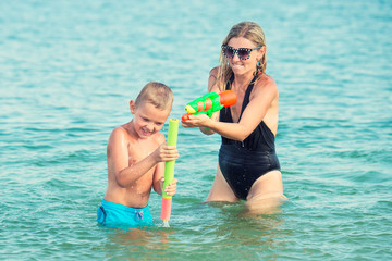 Fototapeta na wymiar Mother and son play on the beach with water pistols. Summer time 