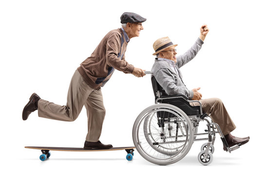 Elderly man on a longboard pushing a man with raised hand in a wheelchair
