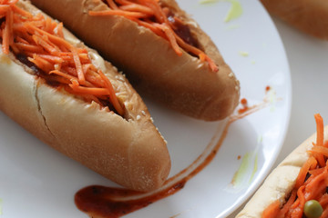 Incredibly delicious and juicy hotdogs with carrots on the white table. 