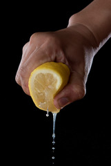 Female hand squeezing half of lemon on black background