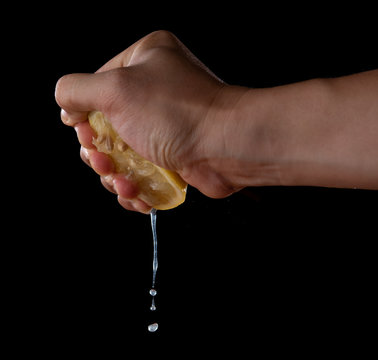 Female hand squeezing half of lemon on black background