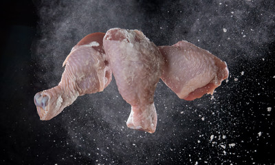 Obraz na płótnie Canvas Chicken leg with flour splash or explosion flying in the air on black background,Stop motion