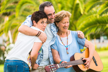 Different mixed ages generations together having fun in familyh portrait leisure activity - old woman play a guitar and laugh a lot - green natural background defocused