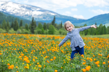 Obraz na płótnie Canvas Little cute baby girl is beautiful and happy, smiling in summer in the meadow against the mountains with snow