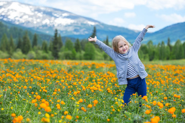Naklejka na ściany i meble Little cute baby girl is beautiful and happy, smiling in summer in the meadow against the mountains with snow