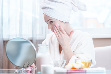 Beautiful young woman applying cream of natural cosmetics on face moisturizing the skin. Hygiene and care for the skin