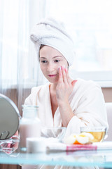 Beautiful happy young woman applying cream on face moisturizing the skin. Hygiene and care for the skin at home