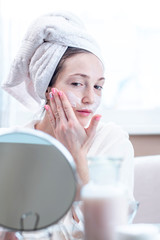 Beautiful happy young woman applying cream on face moisturizing the skin. Concept of hygiene and care for the skin