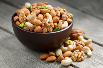 Wooden bowl with mixed nuts on a wooden gray background. Walnut, pistachios, almonds, hazelnuts and cashews, walnut.