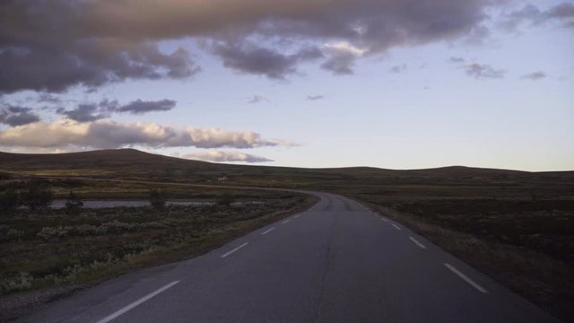 Scenic empty road leading through the Rondane Nationalpark in the Norwegian mountains at sunset in summer.